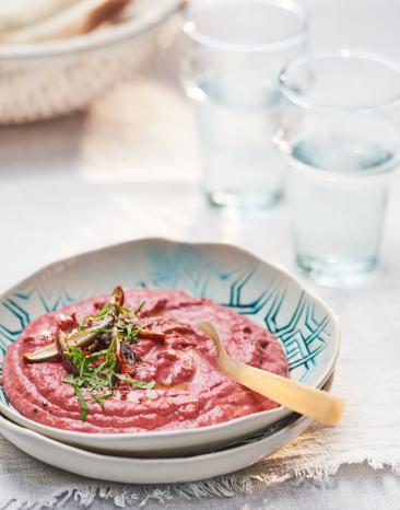 Hummus mit roter Bete mit Kräutern garniert in einer Schale.