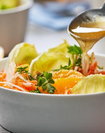 Karottensalat mit Sellerie, Äpfeln und Orangenfilets in einer Schale, wird mit Dressing übergossen.