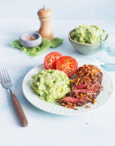 Rumpsteak mit grünem Stampf und Tomatenhälften auf einem Teller. 