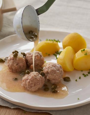 Königsberger Klopse mit Kartoffeln auf einem Teller, Soße wird dazugegeben.