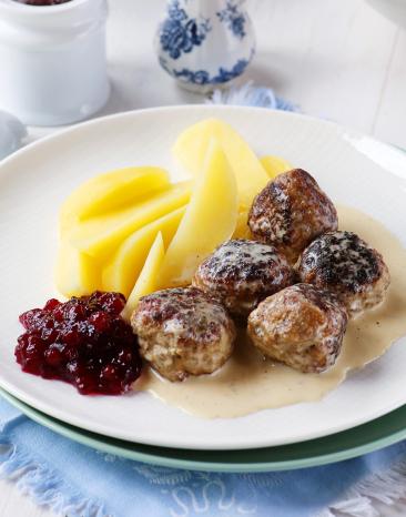 Köttbullar mit Kartoffeln, Sauce und Preiselbeeren auf einem Teller.