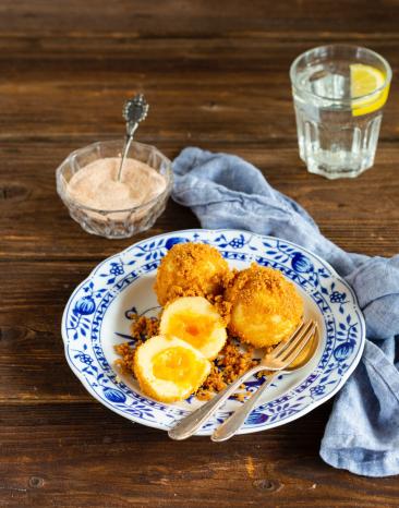 Marillenknödel auf Teller mit Besteck, Zimt-Zucker-Schälchen und Wasserglas mit Zitrone