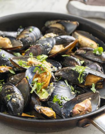 Muscheln in Weißwein (Moules marinières) in einer Schale auf einem Tisch.