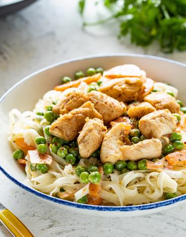 Nudelsalat mit Erbsen und Ingwer-Hähnchen in einem Teller auf einem gedeckten Tisch.