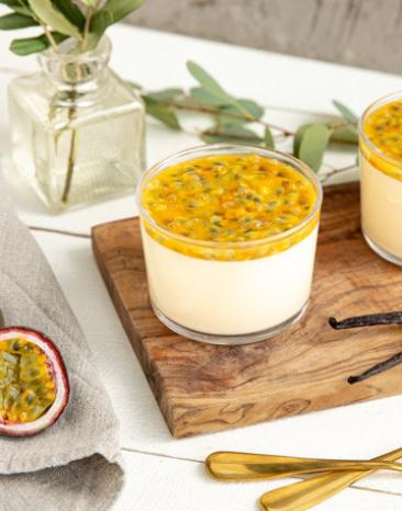 Panna Cotta mit Passionsfrucht und Vanille in zwei Gläschen auf einem Holzbrett.