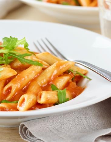 Penne-Pomodoro mit Gorgonzola und Rucola in einem Teller angerichtet.