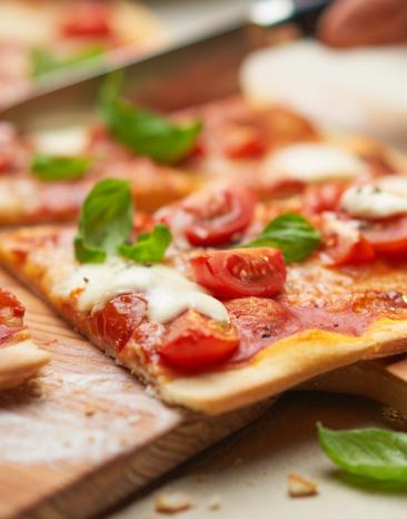 Pizza Margherita angeschnitten auf einem Holzbrett.