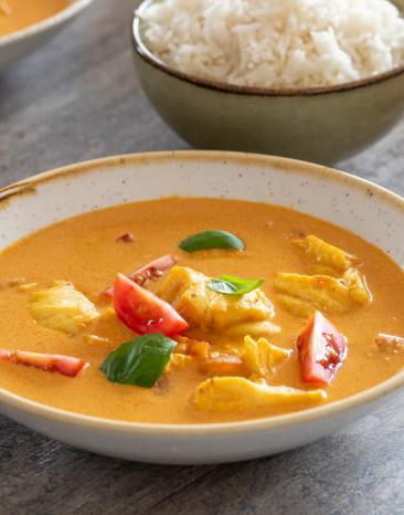 Pochierter Kabeljau mit Tomatencurry daneben Schale mit Reis.