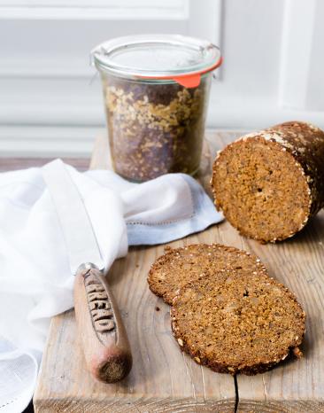 Pumpernickel im Glas, daneben ein Brot in Scheiben geschnitten.