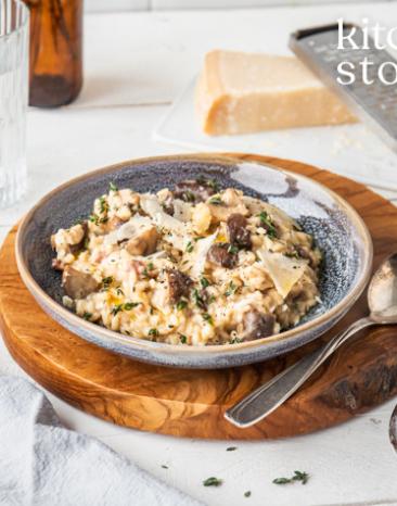 Risotto mit Salsiccia und Pilzen in einem Teller auf einem gedeckten Tisch.