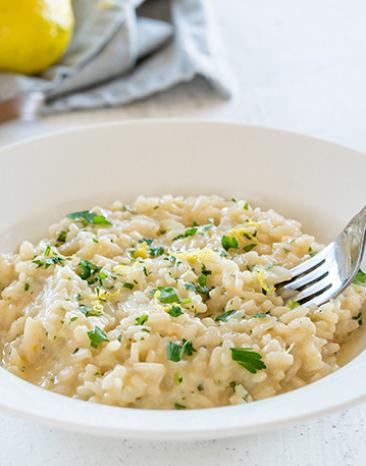 Risotto mit Zitrone und Petersilie wird mit einer Gabel vom Teller genommen.