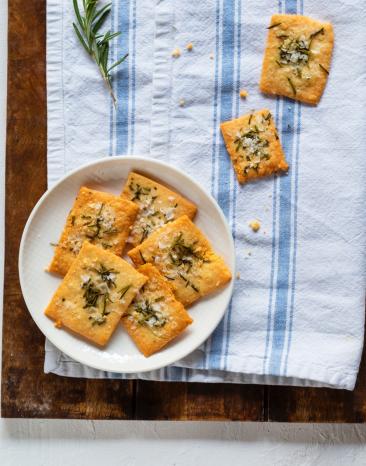 Rosmarin-Cracker auf einem Teller mit Kräutern angerichtet.