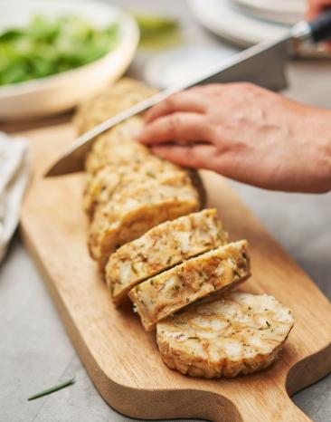 Serviettenknödel wird auf einem Holzbrett in Scheiben geschnitten.