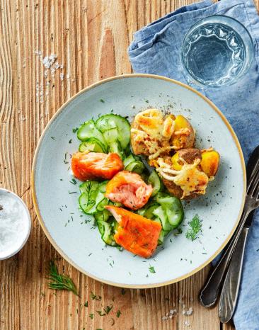 Stampfkartoffeln mit Stremellachs und Gurkensalat auf einem Teller angerichtet. 