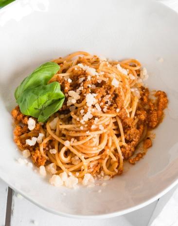 Spaghetti Bolognese auf weißem Teller garniert mit Basilikum.