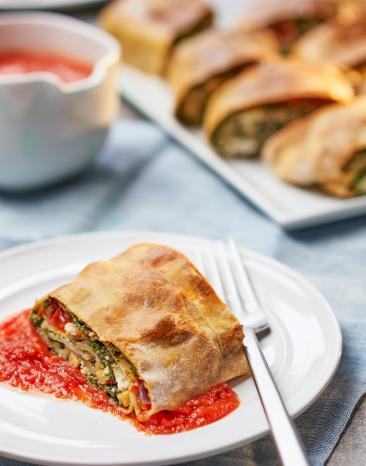 Ein Stück Spinatstrudel mit Tomaten und Schafskäse auf einem Teller.