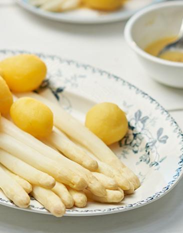 Stangenspargel mit neuen Kartoffeln und Zitronenpfeffer-Butter auf einem Teller.