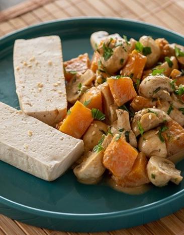 Tofu, gedämpft mit Kürbis und Champignons auf einem Teller.
