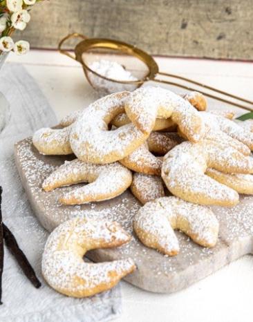 Mehrere Vanillekipferl auf einem Holzbrett.