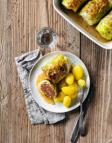 Wirsingrouladen mit Kartoffeln auf Teller und Auflaufform mit Rouladen