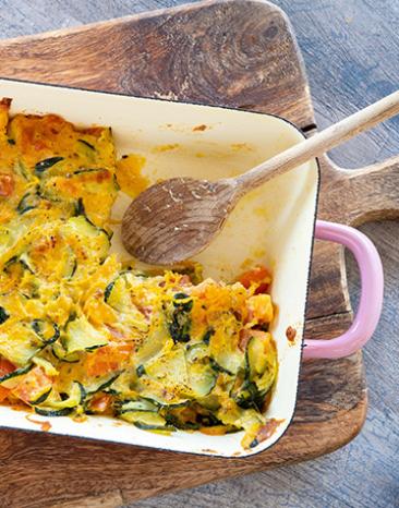 Zucchini-Tomaten-Auflauf in einer Auflauffirm auf einem Holzbrett,