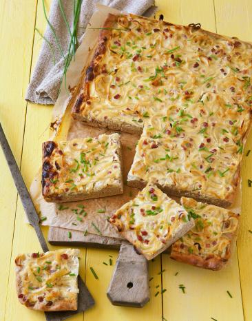 Zwiebelkuchen vom Blech in Stücke geschnitten auf einem Brett.