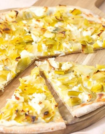 Flammkuchen mit Lauch auf einem Holzbrett.