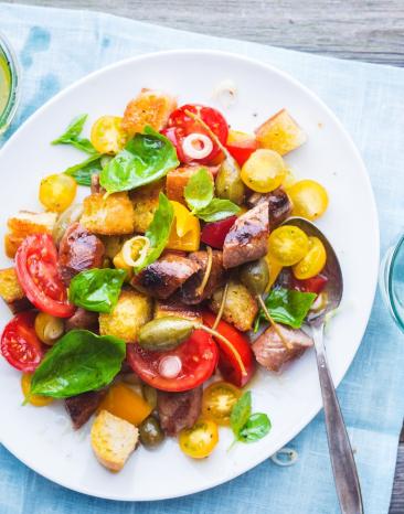 Brotsalat mit gebratener Salsiccia auf einem Teller angerichtet.