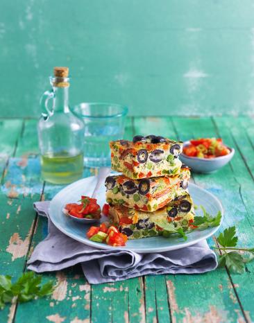 Frittata mit Tomatensalat auf einem Teller gestapelt.