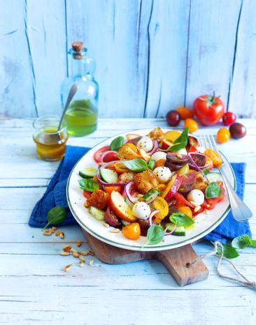 Panzanella mit bunten Tomaten, Mozzarella und Nektarinen auf einem Teller.
