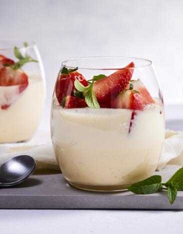 Weiße Creme mit Erdbeeren in zwei Gläsern.