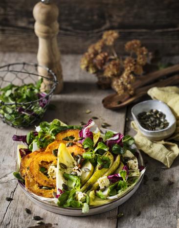 Gebratene Kürbisscheiben auf buntem Herbstsalat.