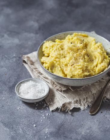 Eine Schüssel mit Kartoffelpüree mit Löffel und Salt daneben.