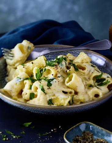Pasta mit cremiger heller Sauce und Gemüse in einer Schale.