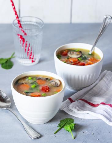 Suppe in Schalen mit Karotten, Pilzen, Erbsen und Tomaten