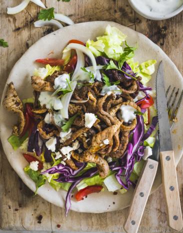 Teller mit Fleisch und Salat auf Holzbrett