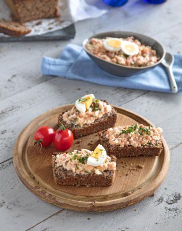 Eier-Tomaten-Aufstrich auf drei Brotscheiben, daneben in einer Schale.