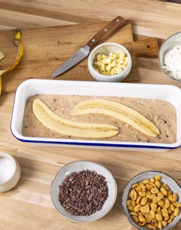 Bananenbrotteig in einer Brotform mit zwei halben Bananen belegt. 