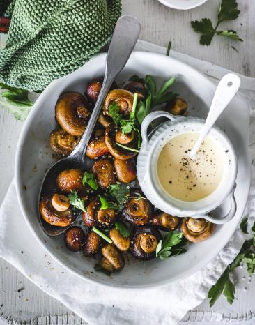Champignons mit Petersilie und Knoblauchsauce auf einem Teller mit Löffel.