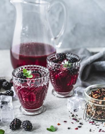 Eistee mit Brombeeren in Gläsern vor einer Karaffe.