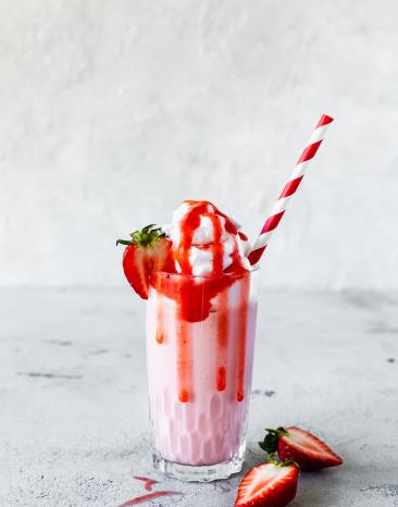 Erdbeer-Milchshake in einem Glas mit Sahne, Erdbeersauce, einer Erdbeere und einem Strohhalm.