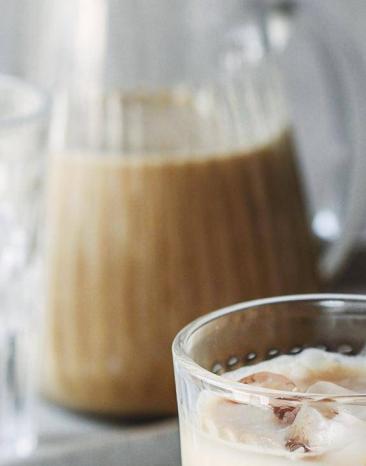 Cremiger Kokosnuss-Eistee in einer Karaffe, daneben ein befülltes Glas mit Eiswürfeln