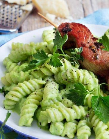 Erbsenfusilli mit gebratenem Lammspieß auf einem Teller, daneben eine Käsereibe und Parmesanstücke