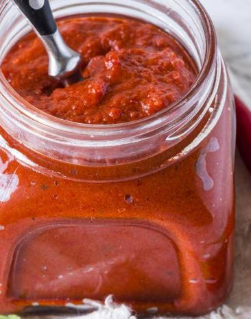 Harissa-Paste in einem Glas, daneben Gewürze auf dem Tisch