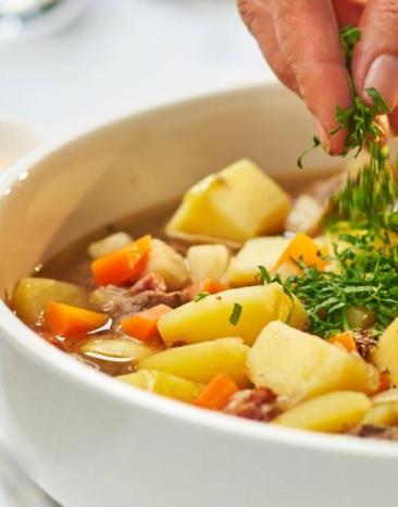 Gulasch aus Kartoffeln und Fleisch in einer Schale wird gerade mit Petersilie dekoriert