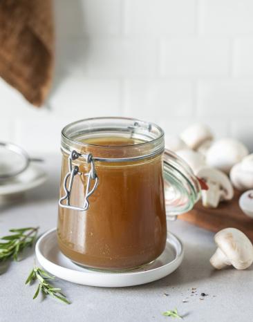 Pilzfond in einem Glas mit Pilzen im Hintergrund.