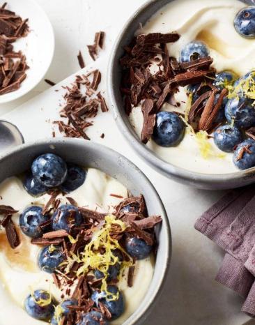 Zwei Schüsseln mit Quarkcreme dekoriert mit Blaubeeren und Schokoraspeln stehen auf einem Tisch