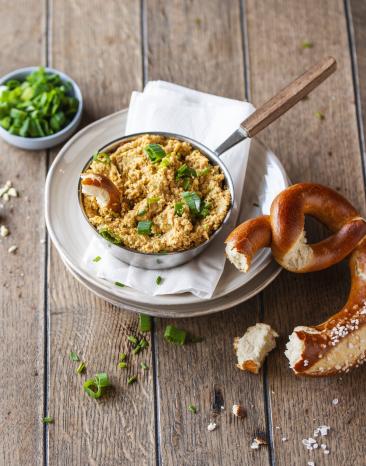 Veganer Obazda in einer kleinen Schale serviert mit Schnittlauch und Laugenbrezel.