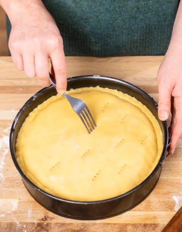 Teig vom gedeckten Apfelkuchen wird vor dem Backen mit einer Gabel eingestochen.