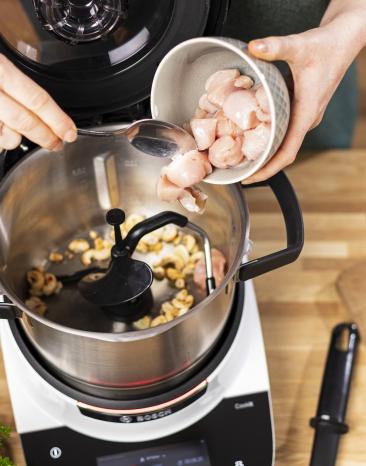 Hähnchenbruststücke werden zu Cashewkernen in den offenen Cookit Kochtopf gegeben